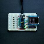 Top-down view of an Arduino setup with a TFT display showing analog voltage readings, wired on a breadboard for testing up to 25V.