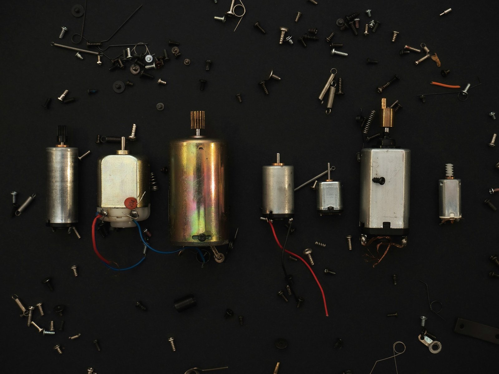 A lineup of various brushed DC motors and parts scattered across a black background, ideal for motor comparison.