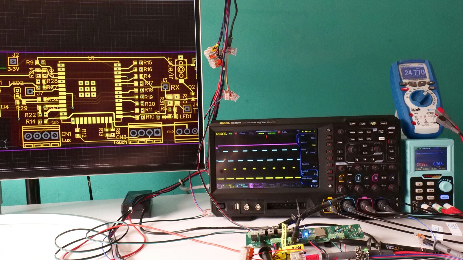 Close-up of a hardware testing desk showing a voltage sensor module wired into a digital oscilloscope and multimeter setup, actively measuring around 25 volts.