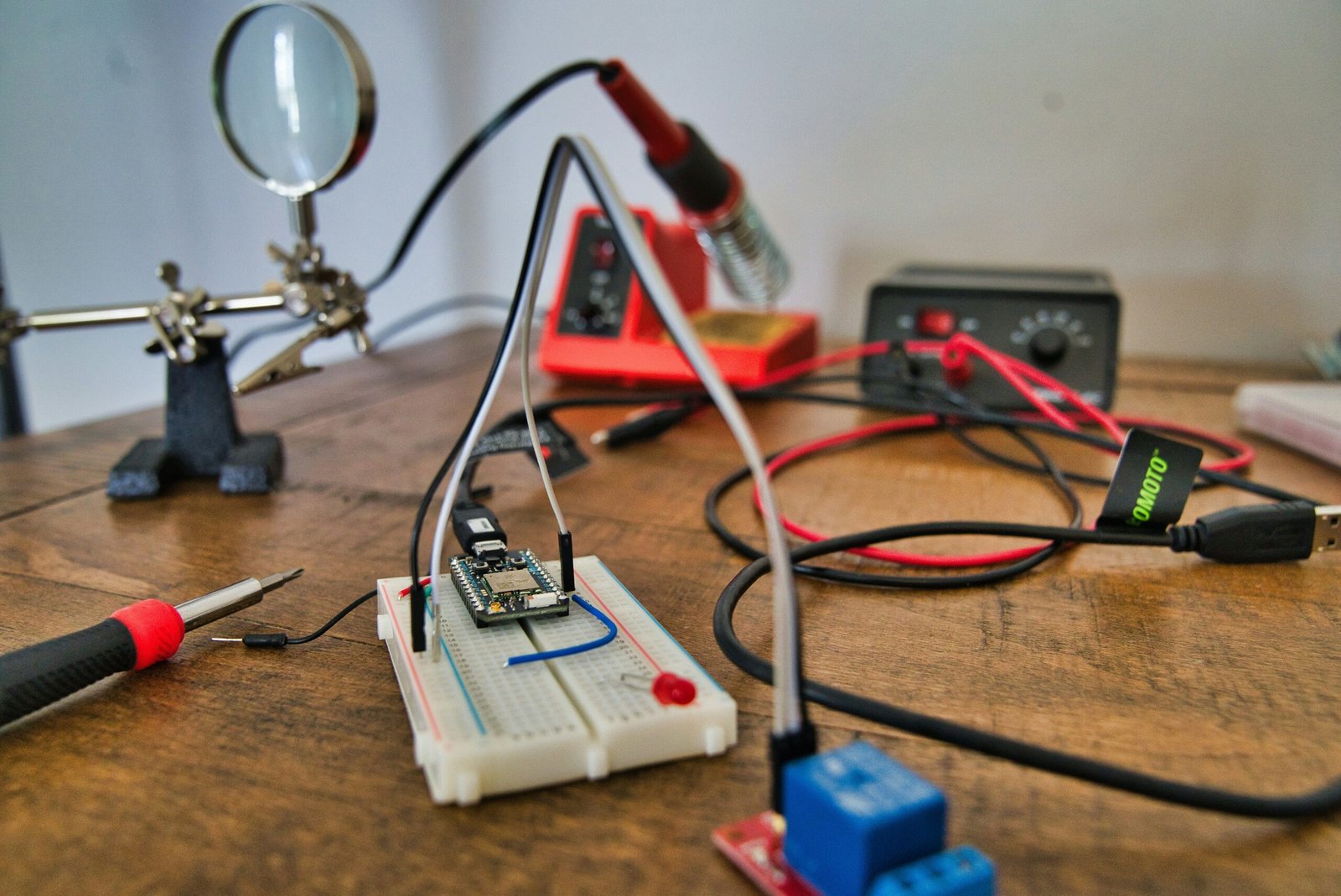 A compact electronics workbench setup featuring a breadboard project with a microcontroller, soldering iron, and magnifier.