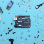 Starter kit of Raspberry Pi Pico components laid out on a blue surface, including resistors, LEDs, jumper wires, and a breadboard ready for prototyping.