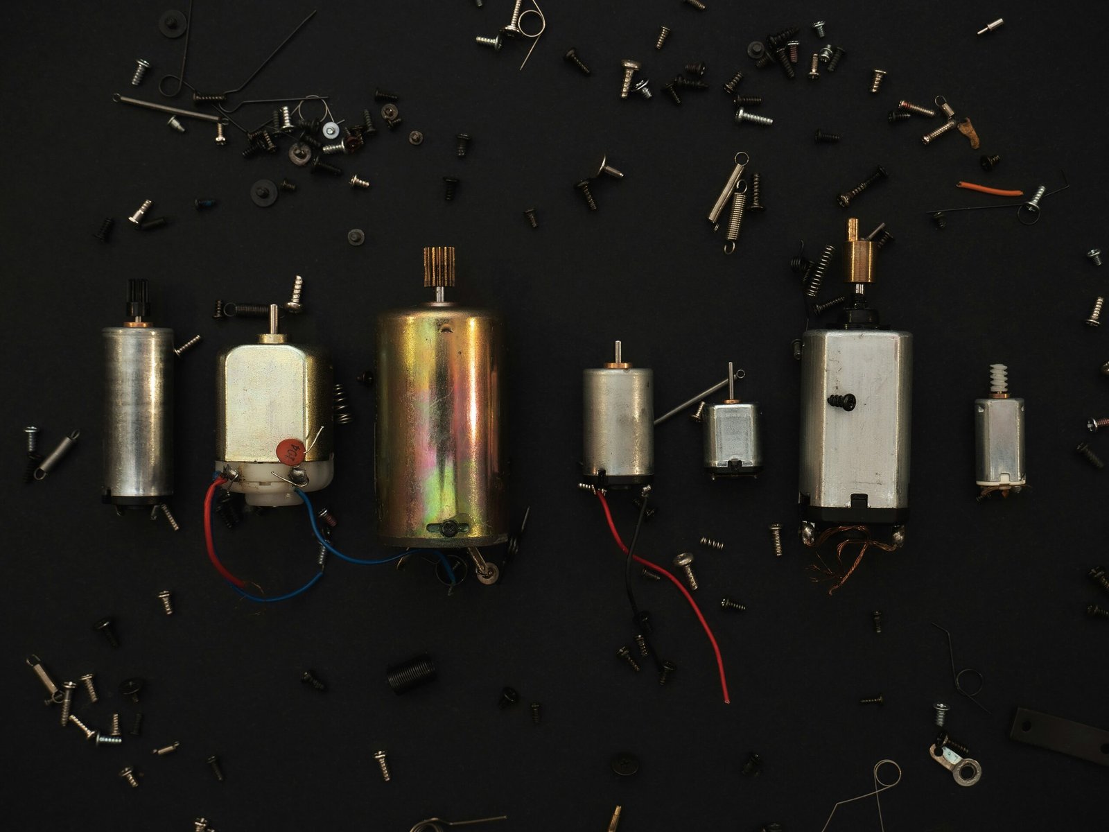 A lineup of various brushed DC motors and parts scattered across a black background, ideal for motor comparison.